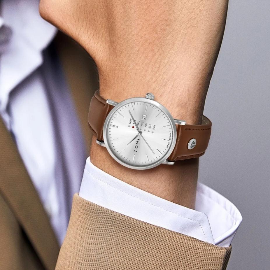 Montre homme TOMI à cadran blanc et bracelet en cuir marron portée avec une veste beige et une chemise blanche